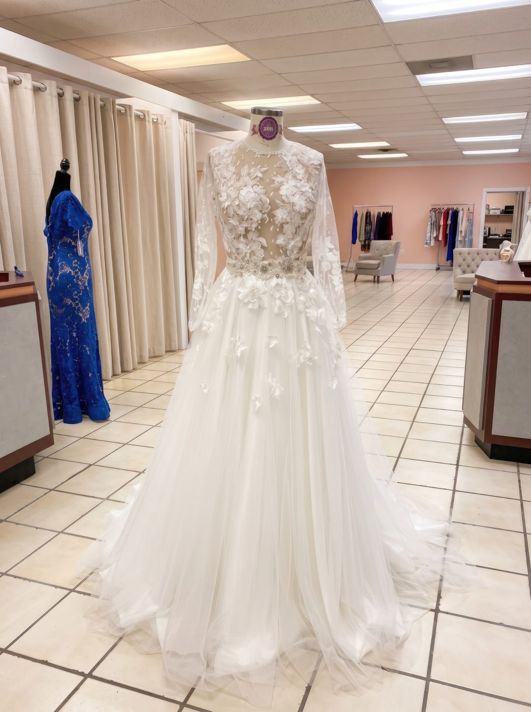 Ivory wedding gown with sheer floral lace sleeves, a beaded waist and a full tulle skirt, displayed in the studio