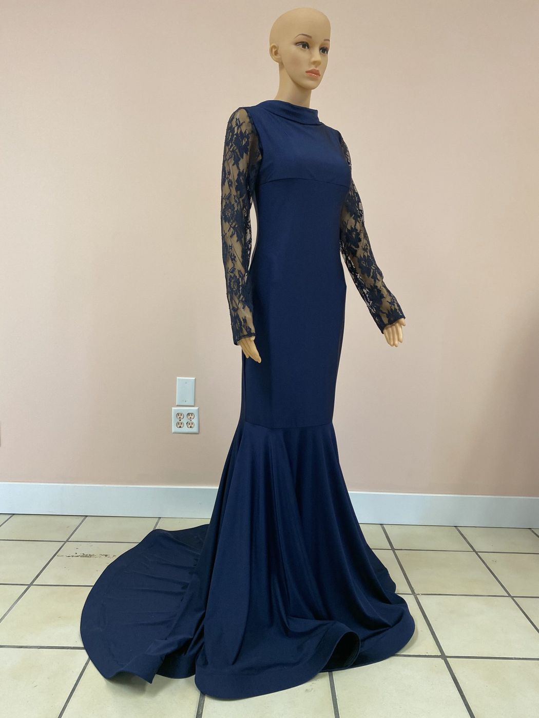 A navy floor-length gown with sheer lace sleeves and a train, on a dress form in the studio