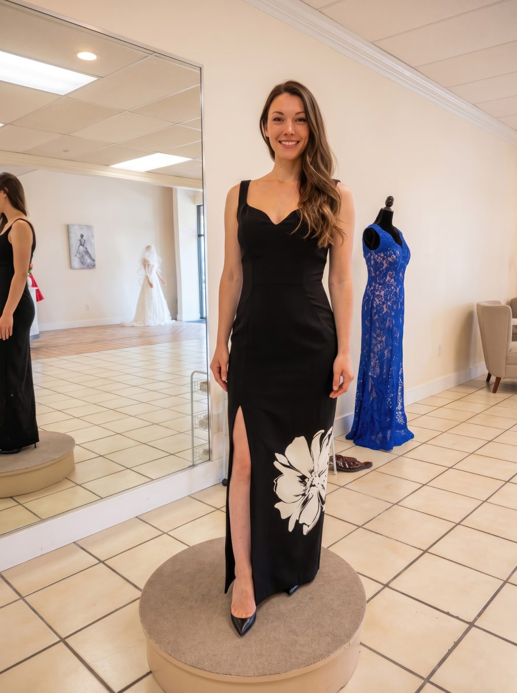 Client in a fitted black evening gown with a side slit and a large white floral print, at a fitting in the studio